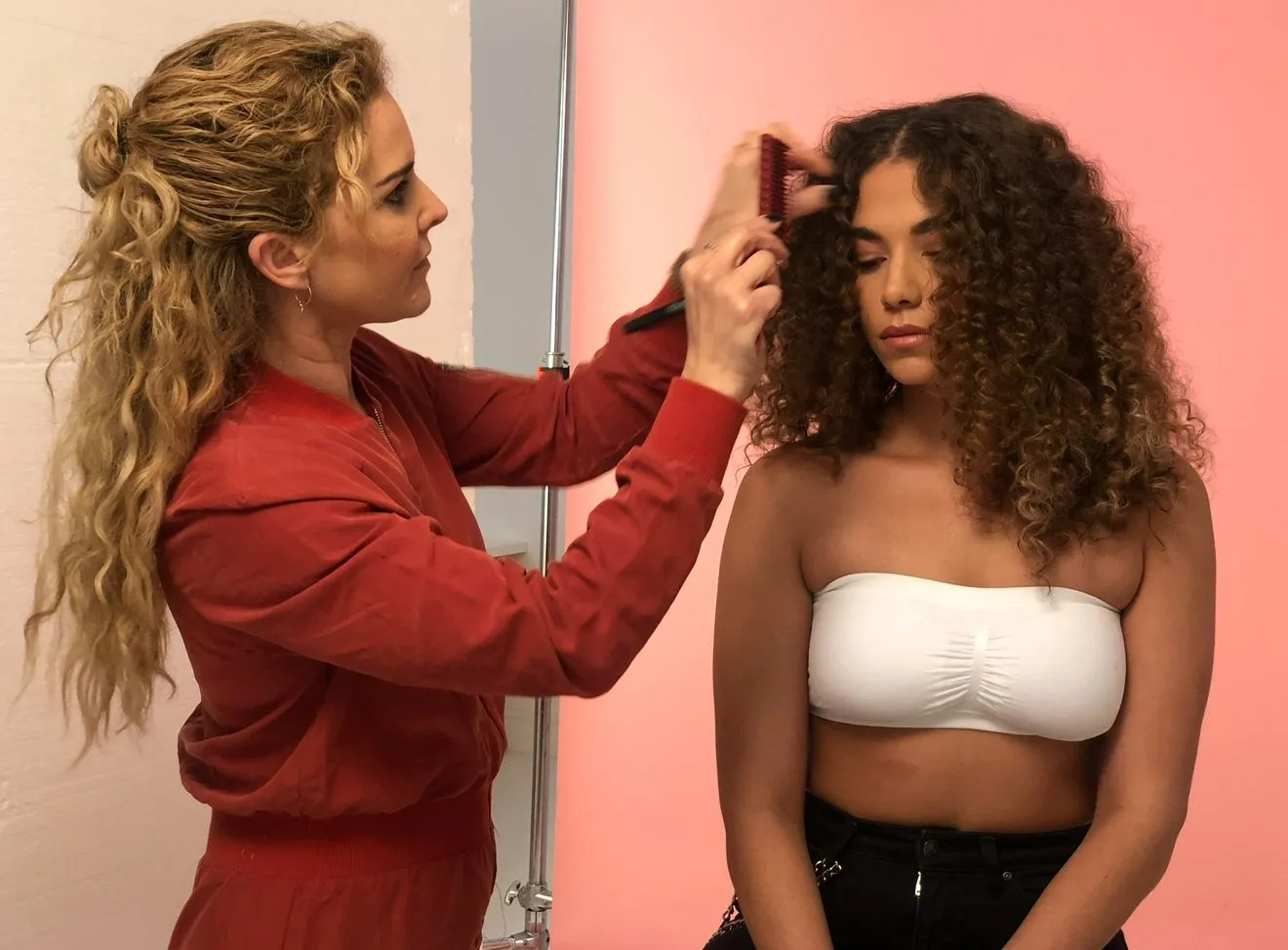 Claire styling a model’s curls with a brush during a PROJECT AFRO shoot against a pink backdrop.